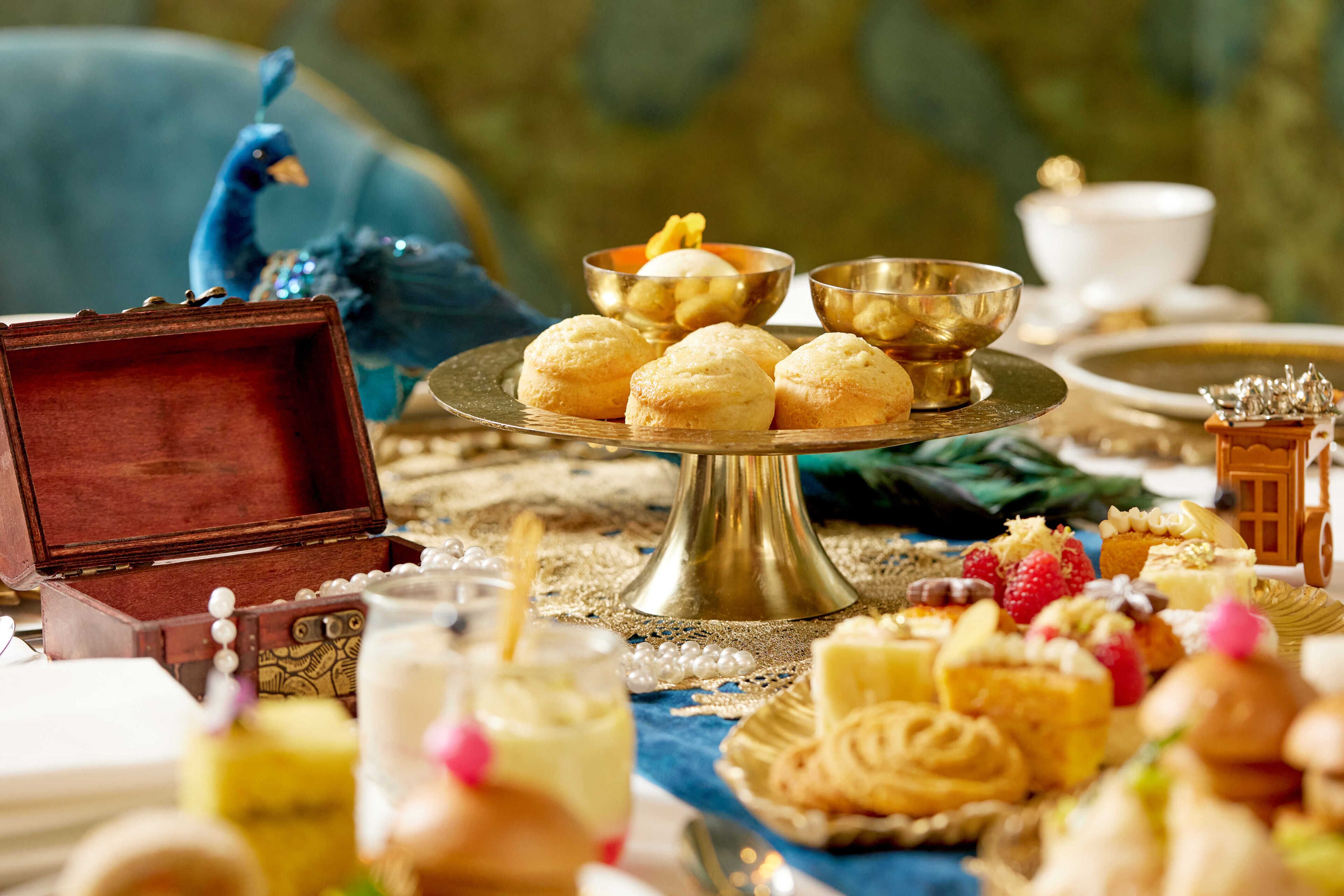 Una mesa dispuesta con diversos pasteles y postres, una figurita de pavo real y un cuenco decorativo.