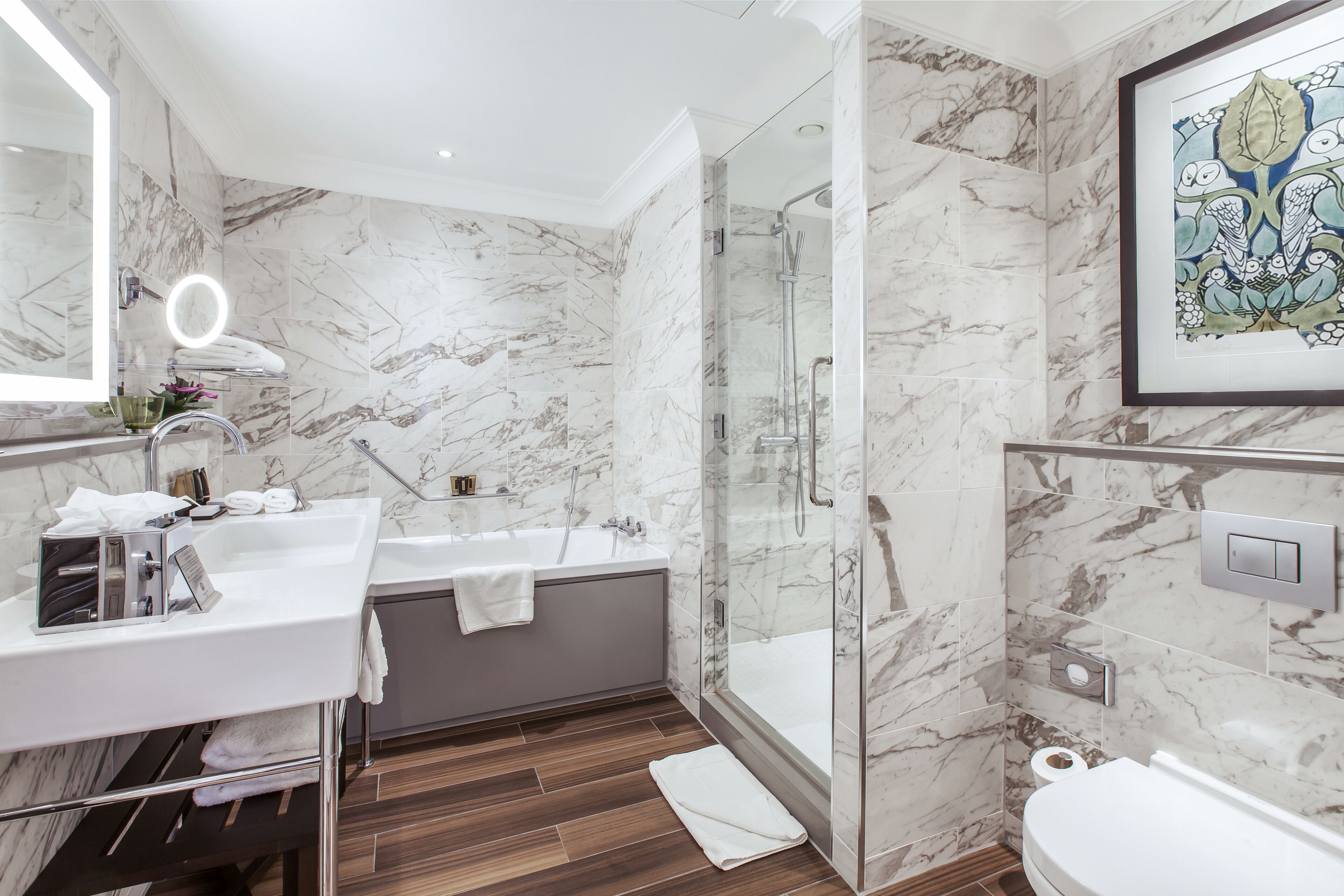 A modern bathroom with a marble wall, a glass-enclosed shower, a white sink, and a toilet.