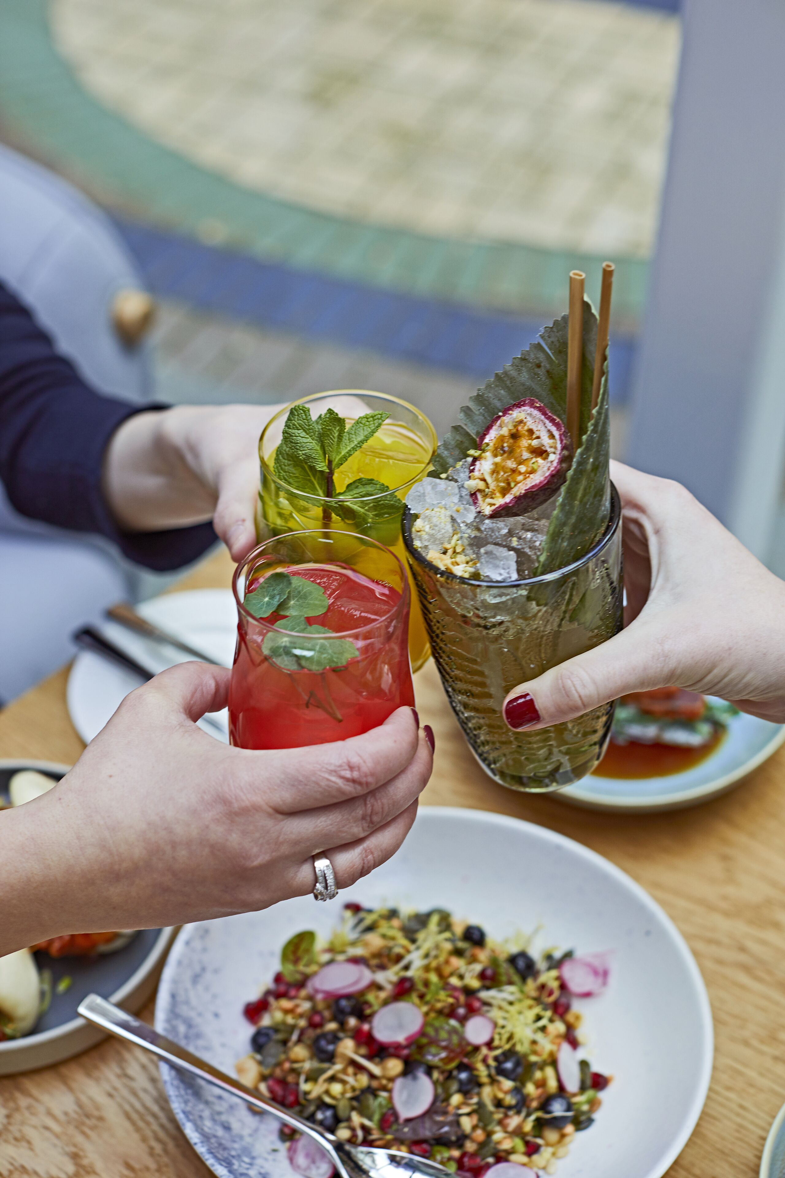 Una persona sosteniendo un vaso con una bebida adornada con una rodaja de fruta y hojas de menta.