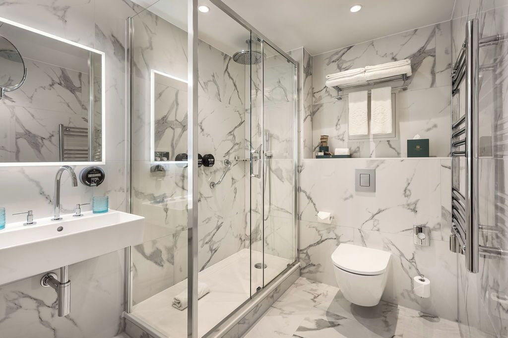 Ein modernes Badezimmer mit einer gläsernen Duschkabine, einem weißen Waschbecken mit Spiegel und einer Toilette.