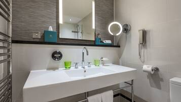 Uma casa de banho moderna com uma sanita, um lavatório branco, copos verdes, um porta-toalhas e um espelho com luz.