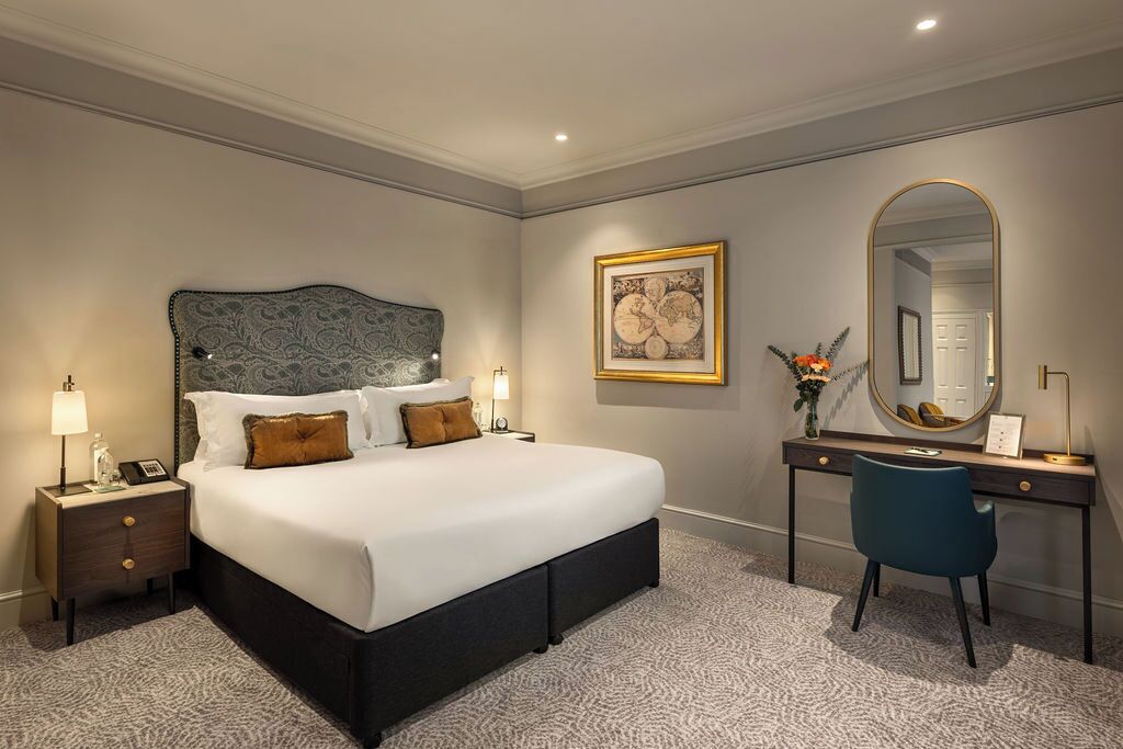 Een keurig opgemaakt slaapkamer met een groot bed, nachtkastjes, een bureau en een spiegel.