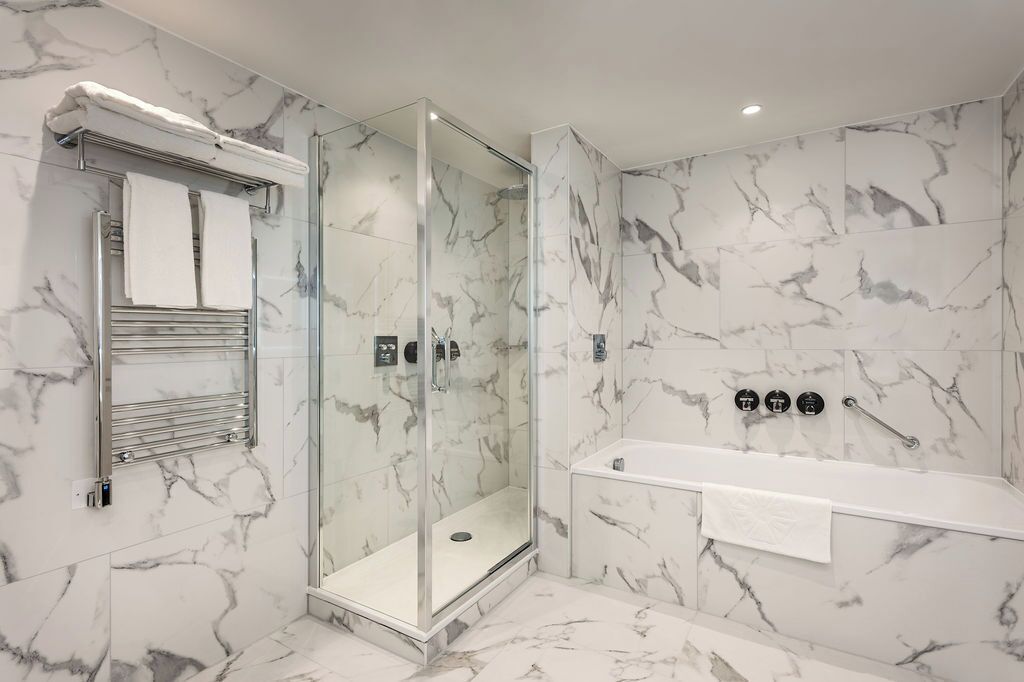 A modern bathroom with a glass-enclosed shower, a white bathtub, and marble walls.
