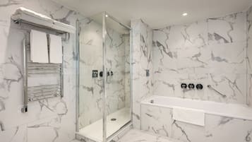 A modern bathroom with a glass-enclosed shower, a white bathtub, and marble walls.