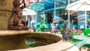 A fountain with a bronze statue, a birdcage with flowers, and a glass building in the background. - St. James' Court, A Taj Hotel, London (London)