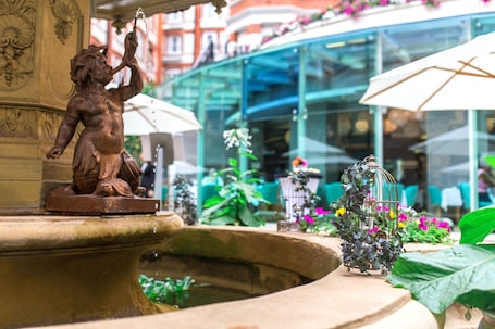 A fountain with a bronze statue, a birdcage with flowers, and a glass building in the background.