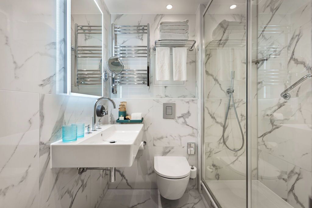 A modern bathroom with a marble backsplash, a white sink with a mirror, a glass shower enclosure, and a toilet.