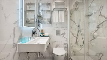 A modern bathroom with a marble backsplash, a white sink with a mirror, a glass shower enclosure, and a toilet.