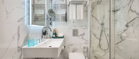Un baño moderno con salpicadero de mármol, un lavamanos blanco con espejo, cabina de ducha de cristal y un inodoro.