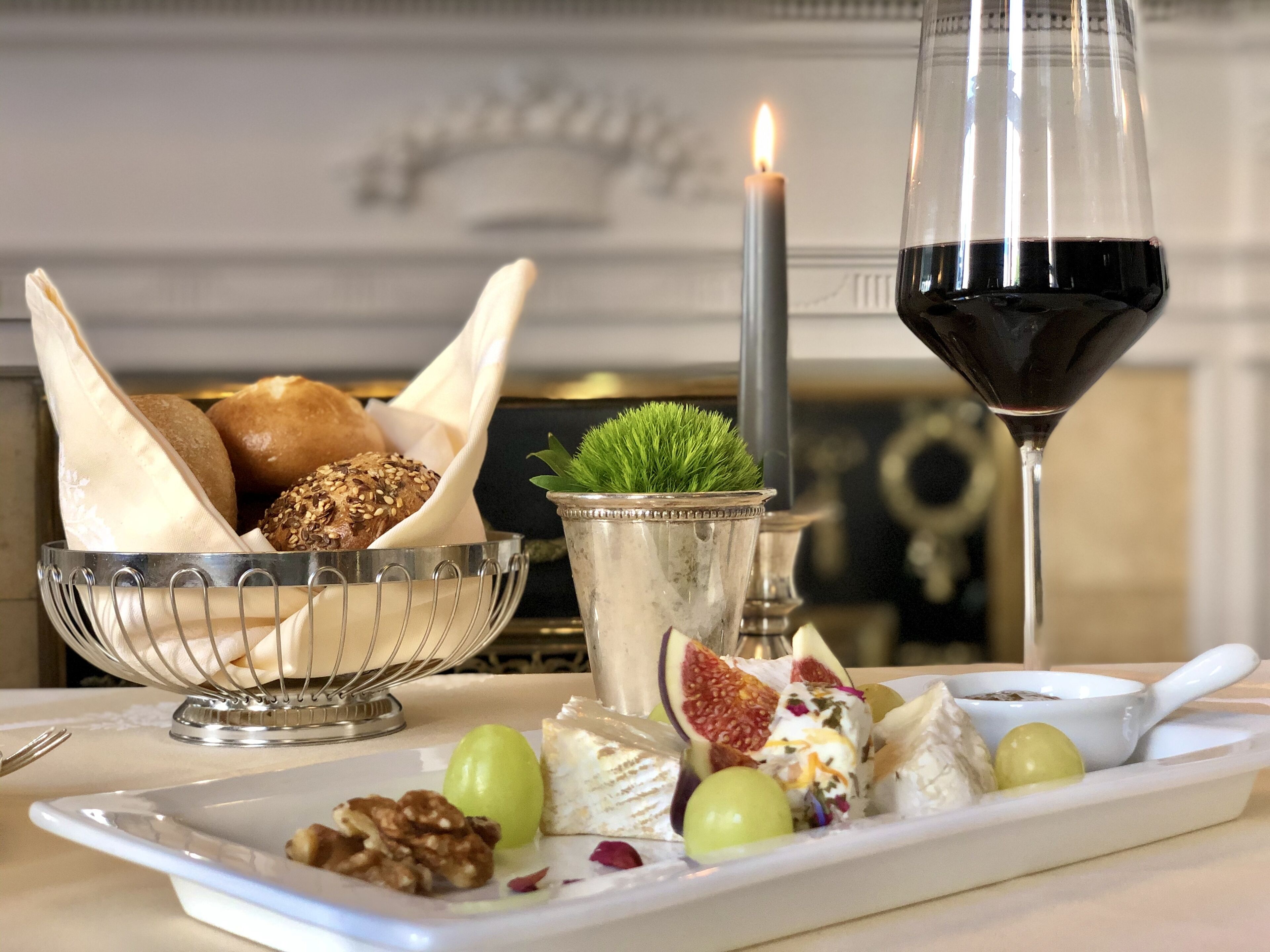 Una mesa de comedor con una variedad de panes, una vela, una copa de vino tinto y un plato con frutas y frutos secos.