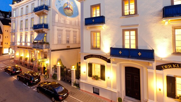 Un hôtel à la façade illuminée par la lumière de la lune, doté de nombreux balcons et d’une enseigne bien visible.