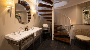 Une salle de bain moderne avec un double lavabo, un miroir et un escalier menant à un niveau supérieur.