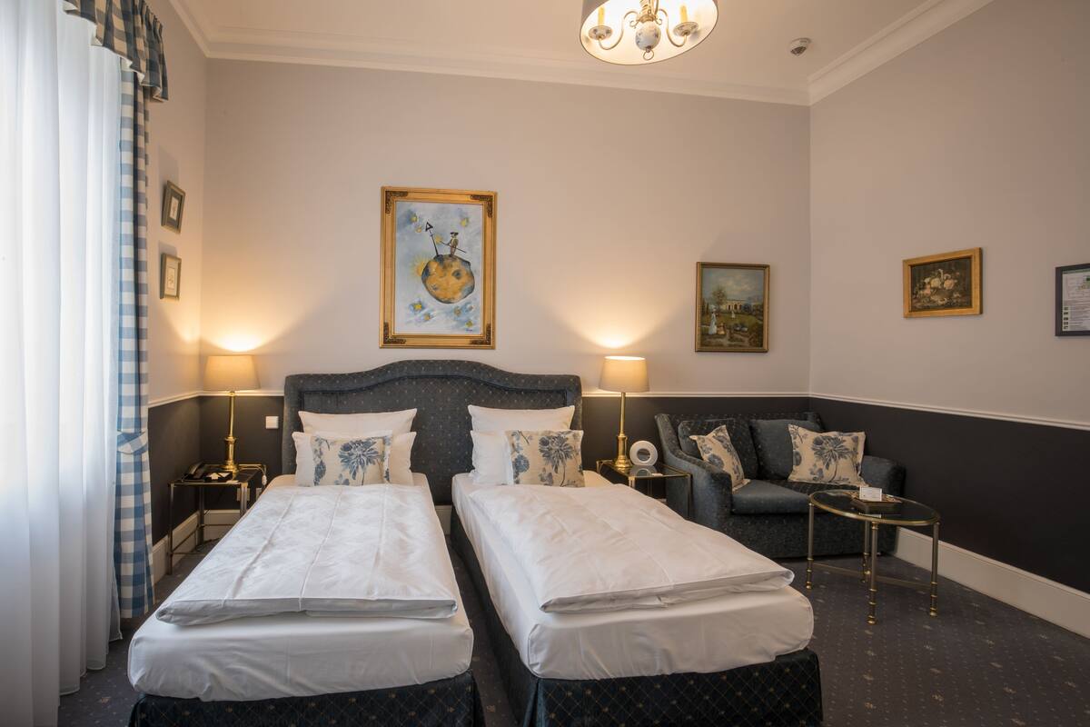 Une chambre d’hôtel avec deux lits, un canapé, un lustre et des œuvres d’art accrochées aux murs.