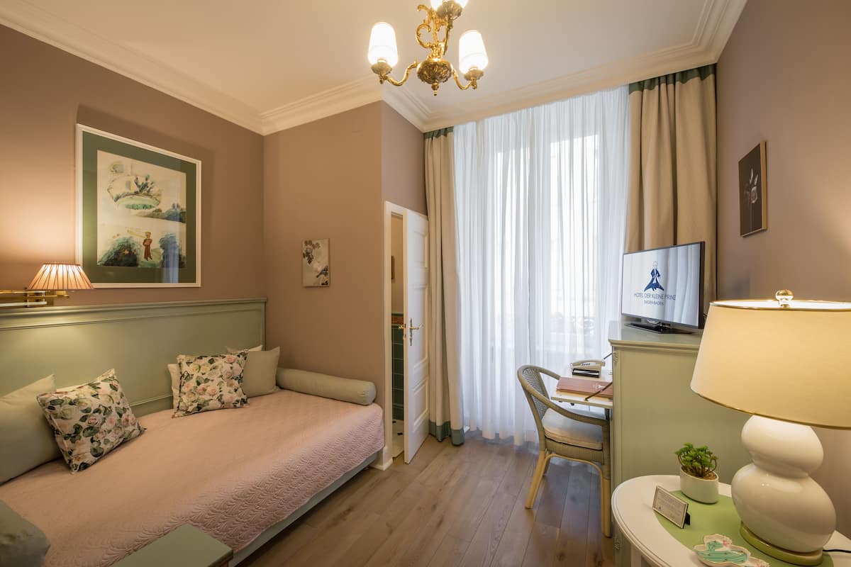 Une chambre d’hôtel comprenant un lit, un bureau avec une chaise, une télévision et une fenêtre avec des rideaux.
