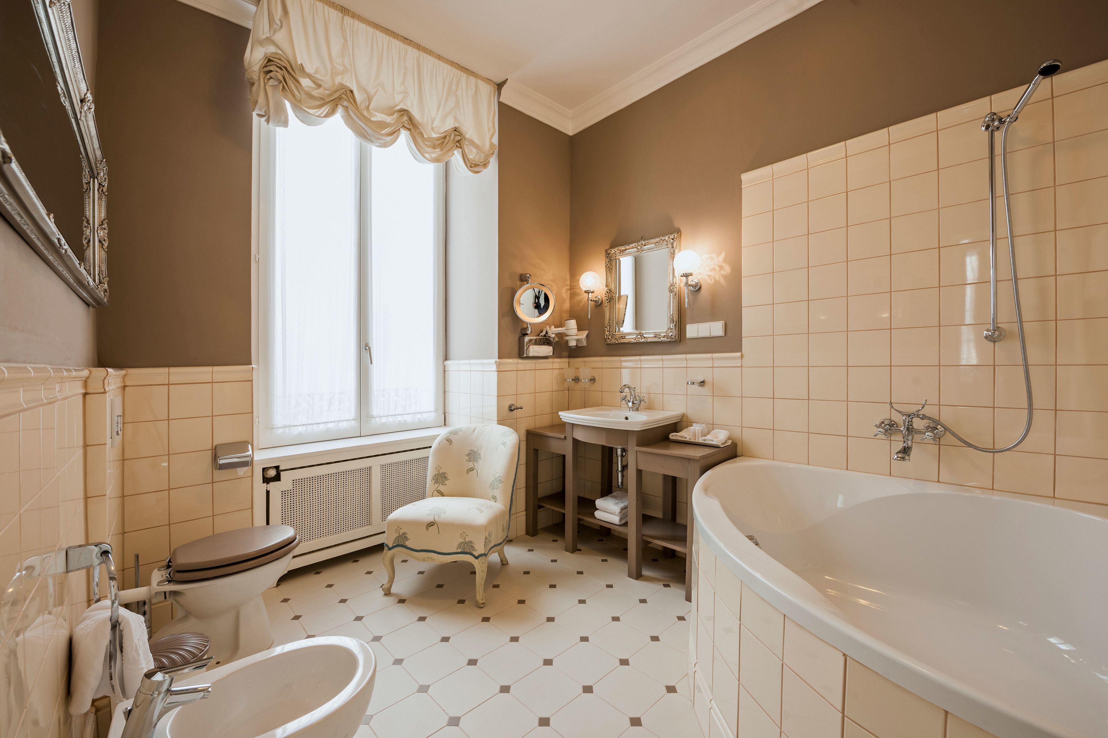 A bathroom with a toilet, a sink, a chair, a bathtub, and a window with curtains.