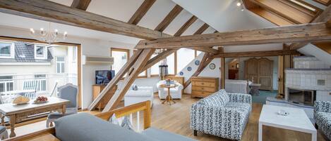 Ein großzügiges Loft mit freiliegenden Holzbalken, einem Essbereich, einer Couch, einem gemusterten Sessel und einem Kamin.