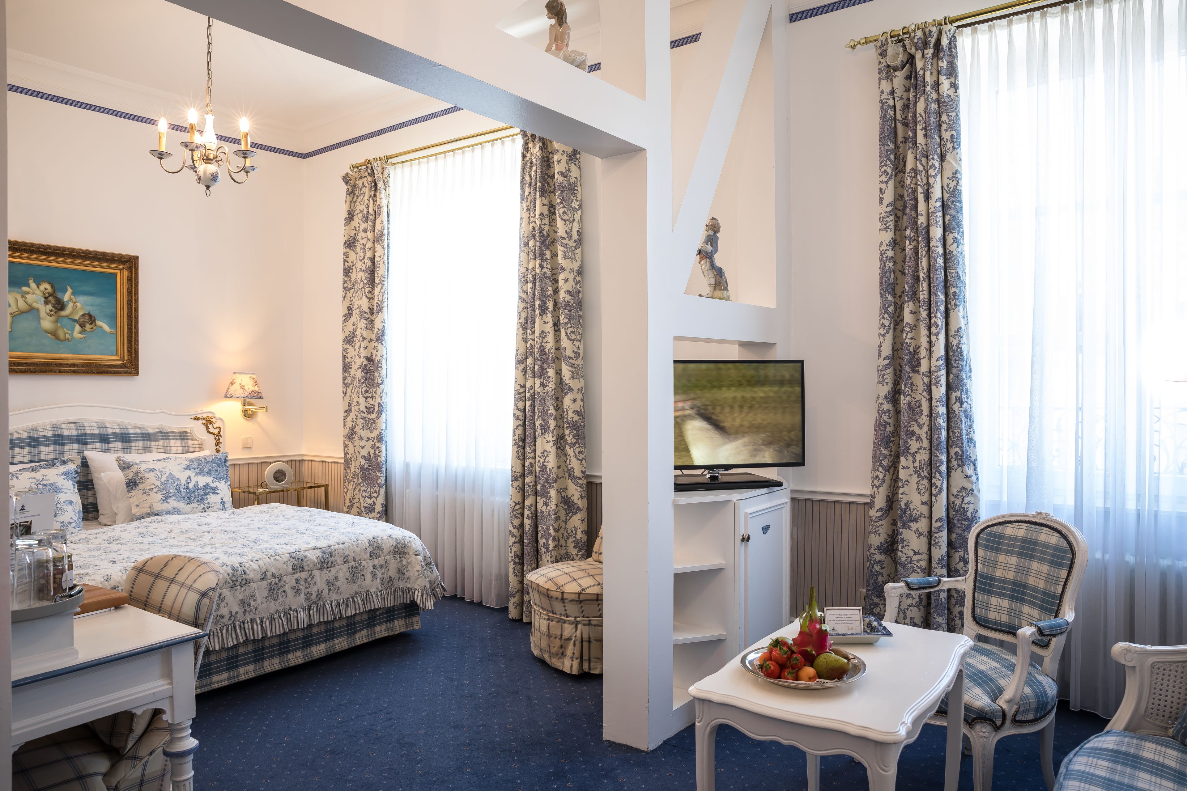 A hotel room with a bed, a desk, a chair, a television, and a table with fruit.