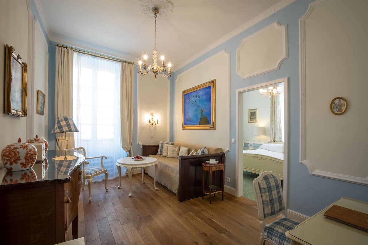 Une pièce avec un plancher en bois, un canapé, une petite table ronde, une chaise, une commode et un miroir.