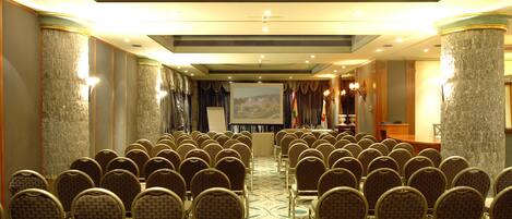Un salón de conferencias con filas de sillas, un atril y una pantalla al frente.