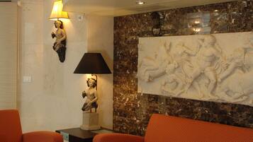 Una sala de estar moderna con techo curvo, pared de mármol con escultura en relieve, sofá naranja, mesa de centro negra con revistas y una lámpara de pie.