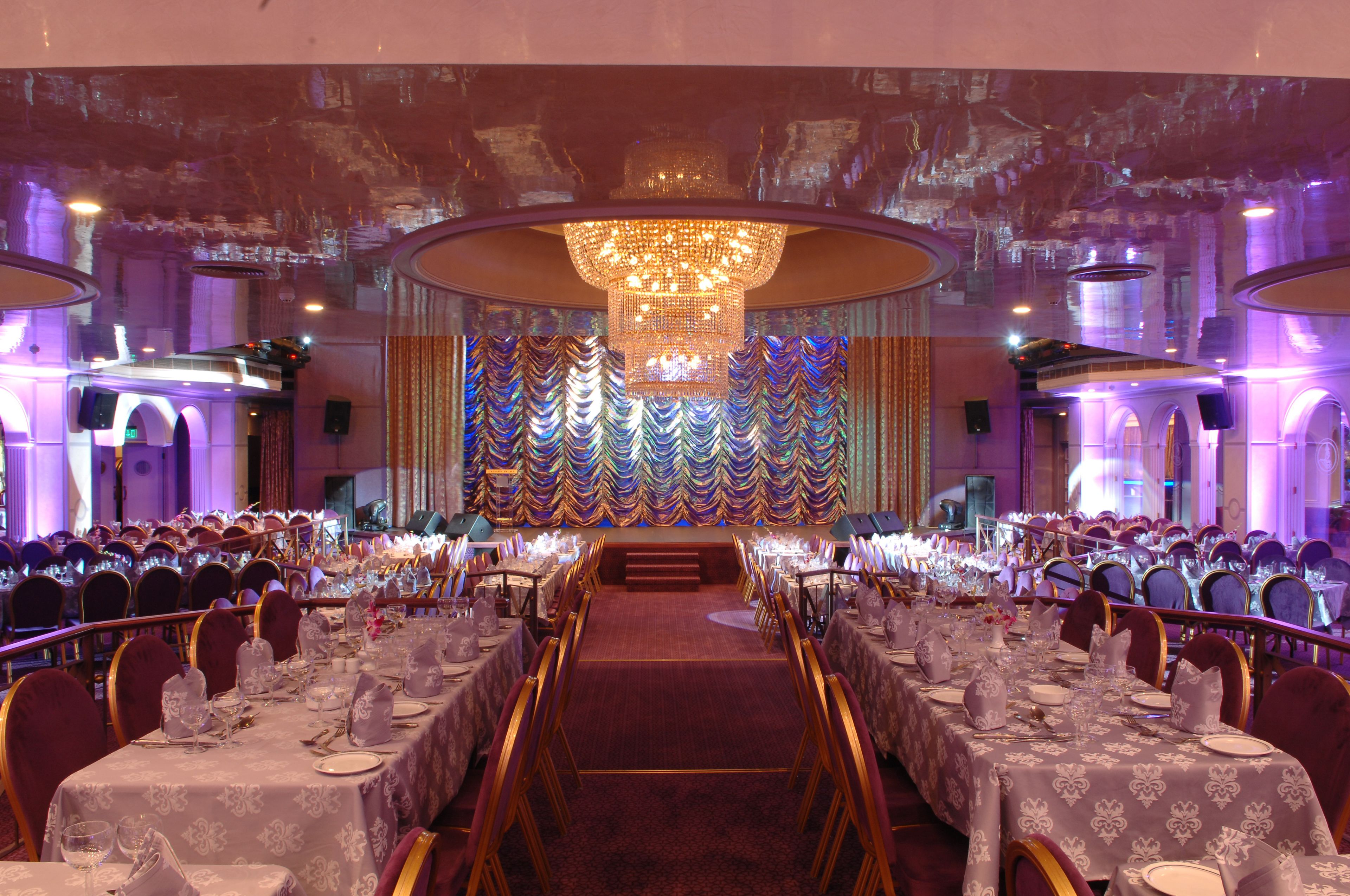 A banquet hall with round tables, a central stage, and a decorative backdrop.