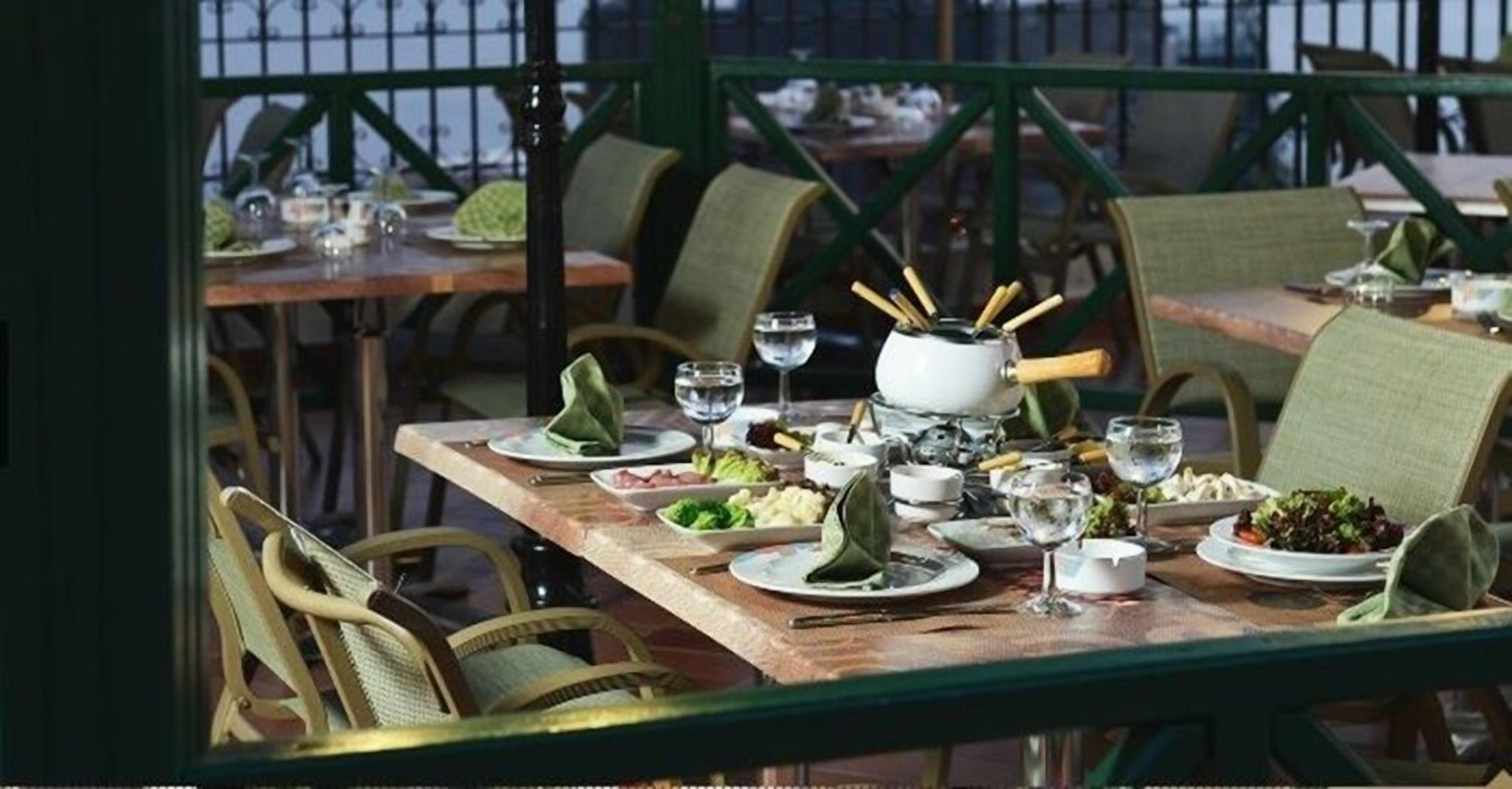 Une table à manger dressée avec des assiettes, des verres et une théière, entourée de chaises en osier.