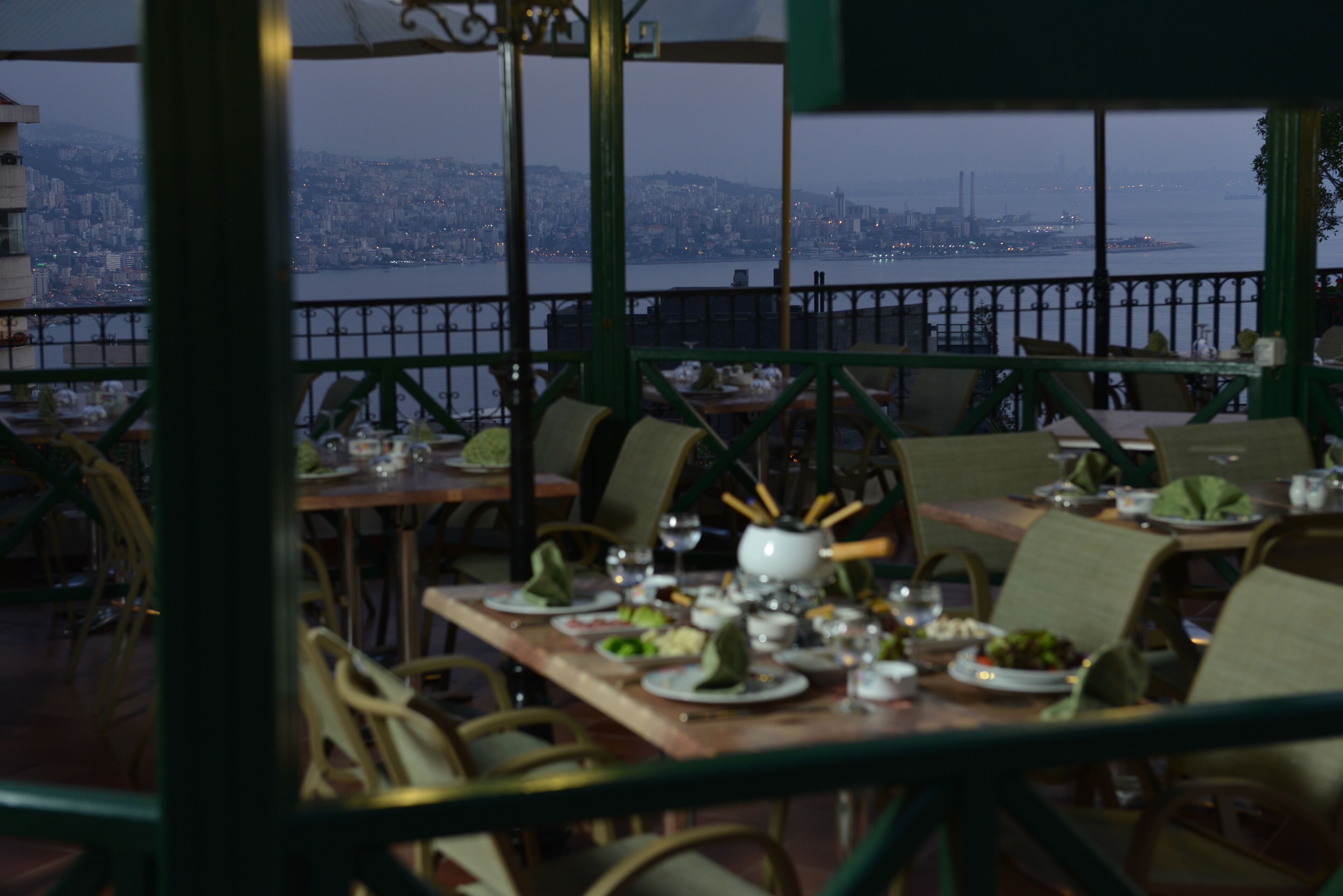 A restaurant with tables set for dining, chairs, and a view of a cityscape across a body of water.
