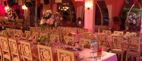 Un salón de banquetes con mesas redondas dispuestas para comer, cada una con centros de flores y cubertería.