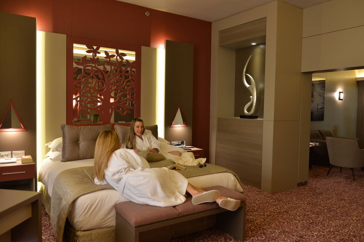 Ein modernes Hotelzimmer mit einem großen Bett, einer dekorativen Wandverkleidung und einer Sitzecke mit Tisch und Stühlen.