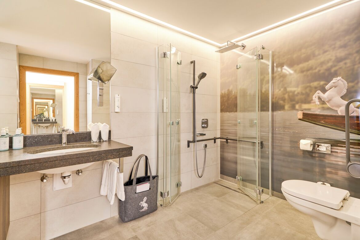 Un baño moderno con ducha de vidrio, un espejo grande y tocador con lavamanos y perchero para toallas.