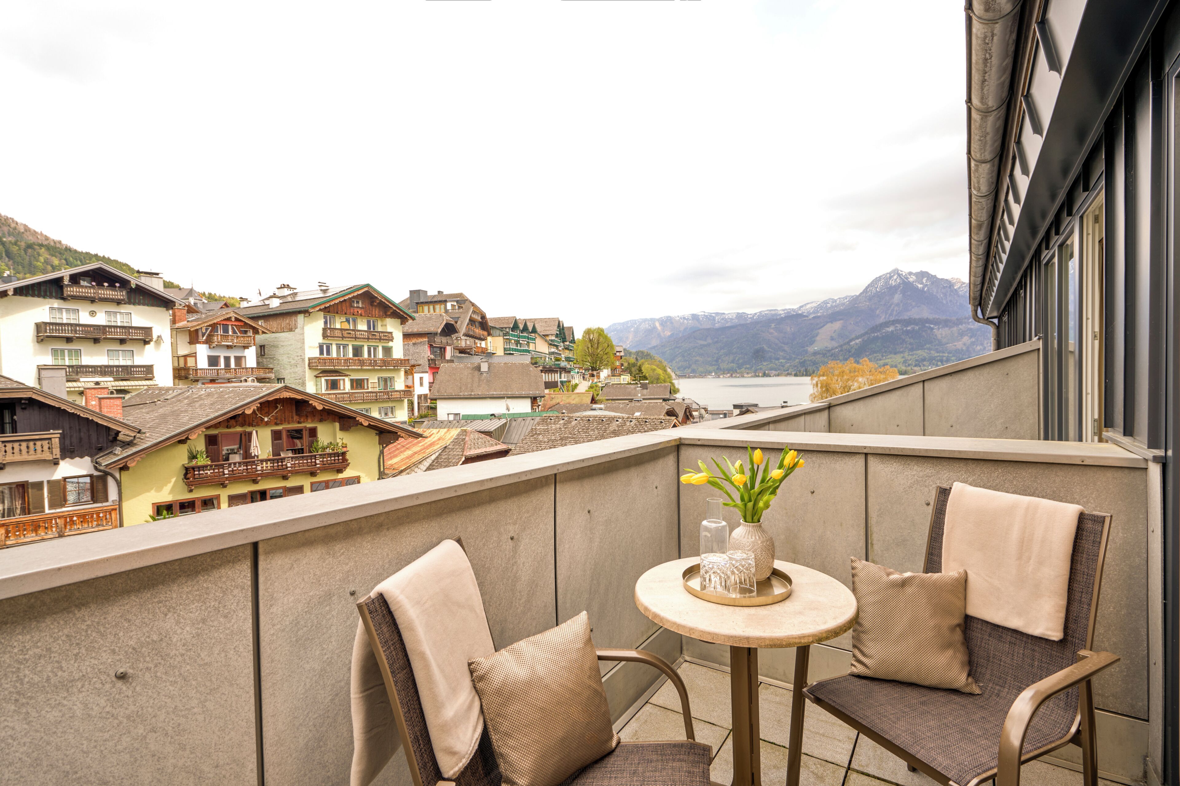 A balcony with two chairs and a table, overlooking a mountainous landscape and a body of water.