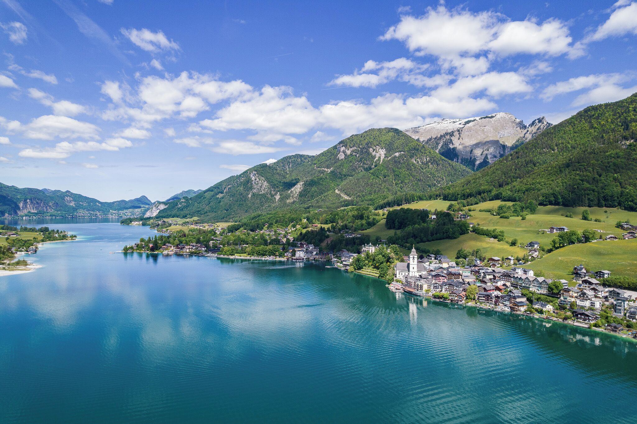 A lakeside town with a church, houses, and mountains in the background.