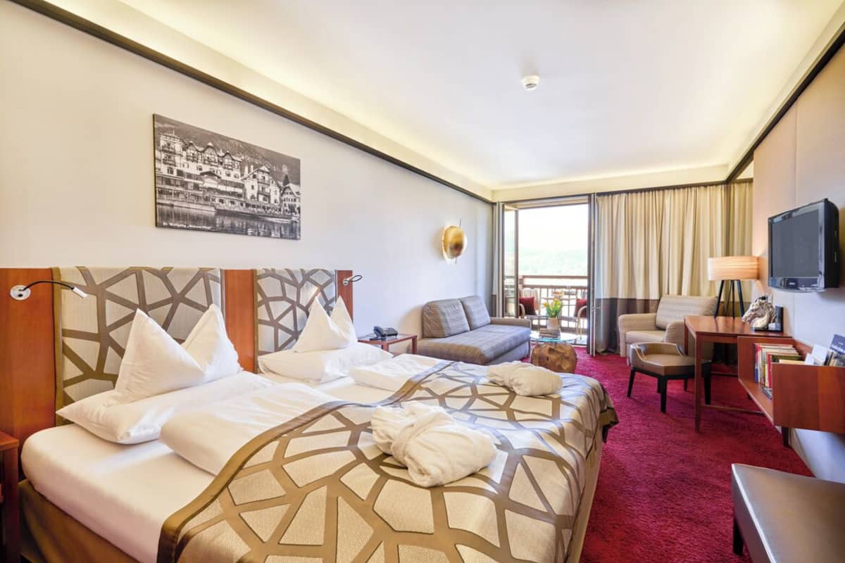 A hotel room with two beds, a sofa, a desk, a television, and a large window.