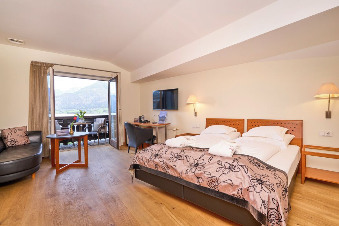 A hotel room with a bed, a desk, a chair, a sofa, and a balcony with a view.