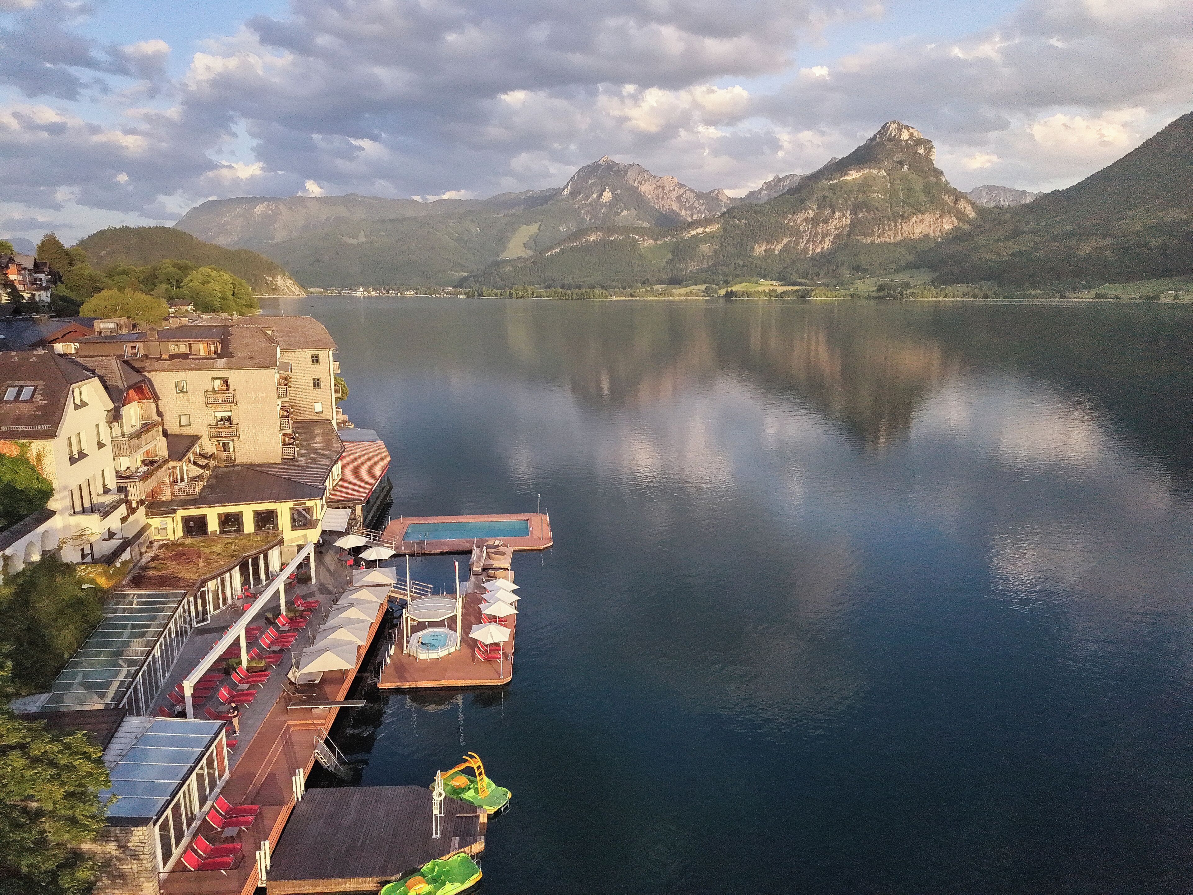Hotel frente a un lago con muelle, asientos al aire libre y vistas a la montaña.