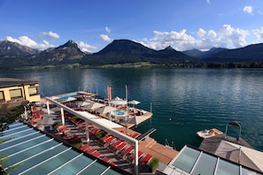 A lakeside hotel with a pool, sun loungers, and a boat dock.