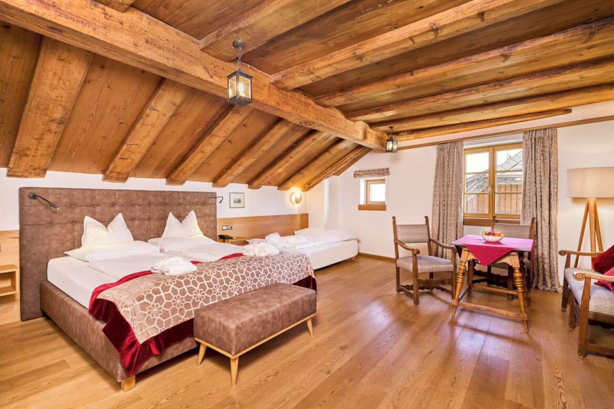 A bedroom with a wooden ceiling, a bed with white bedding, a small table with a red tablecloth, and a chair.