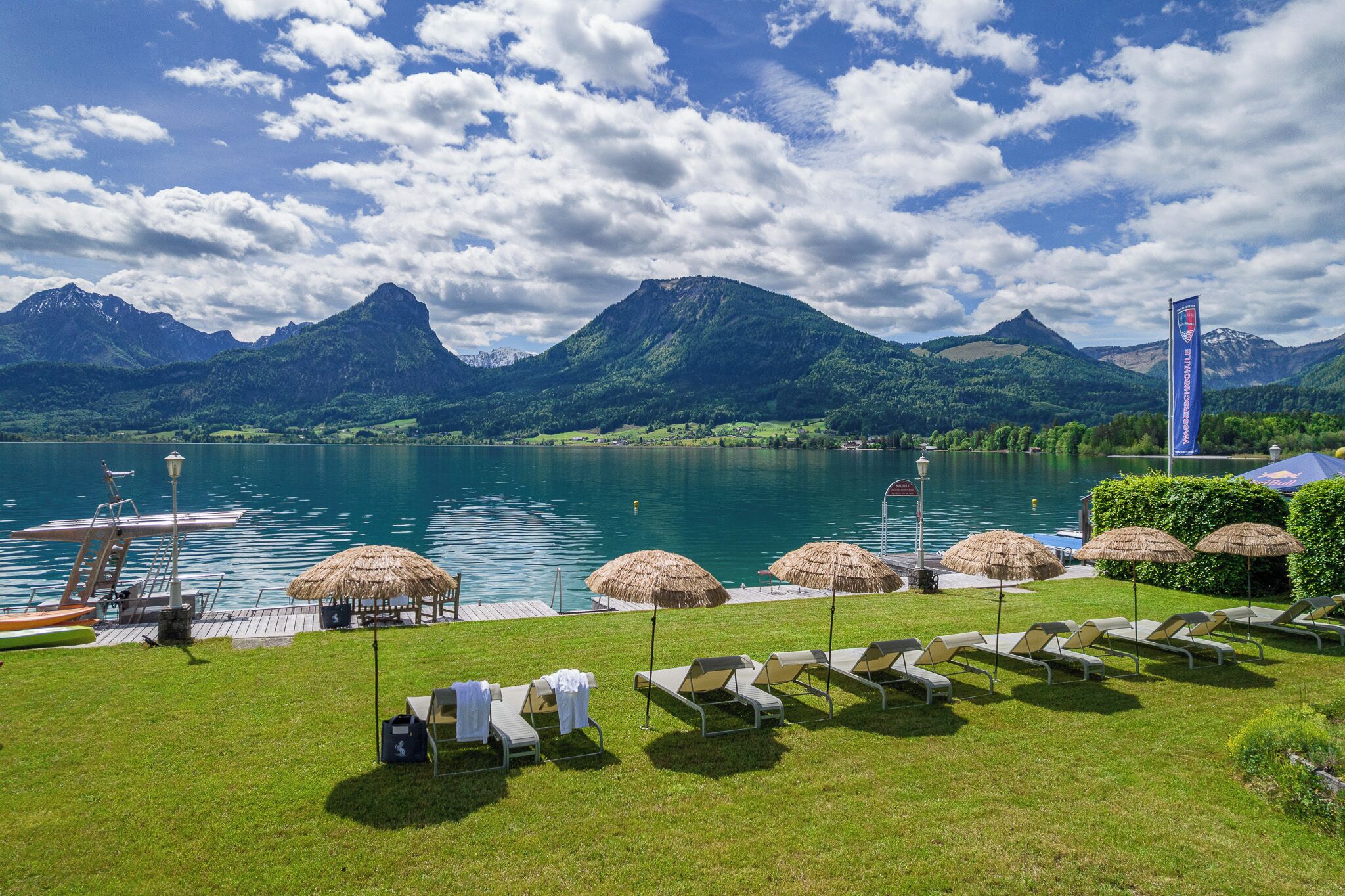 Un resort junto al lago con sillas de descanso, sombrillas de paja y un muelle.