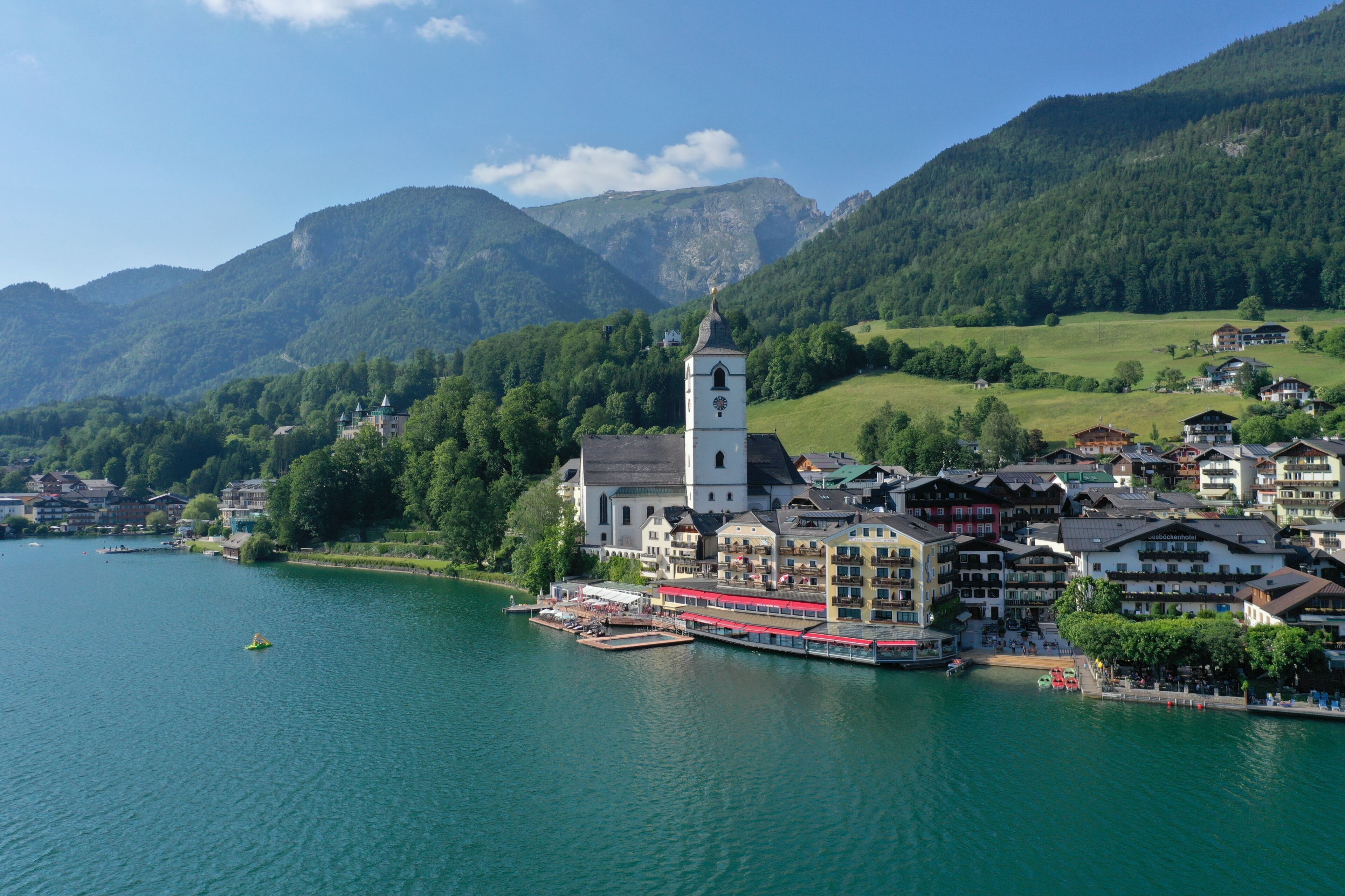 A lakeside town with a prominent church, a boat dock, and surrounding greenery.