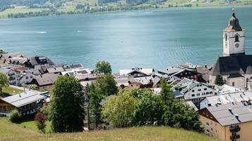 Une personne se tient sur une colline herbeuse, d’où elle a une vue sur un lac, avec des montagnes en arrière-plan et une ville où l’on aperçoit des bâtiments et le clocher d’une église.