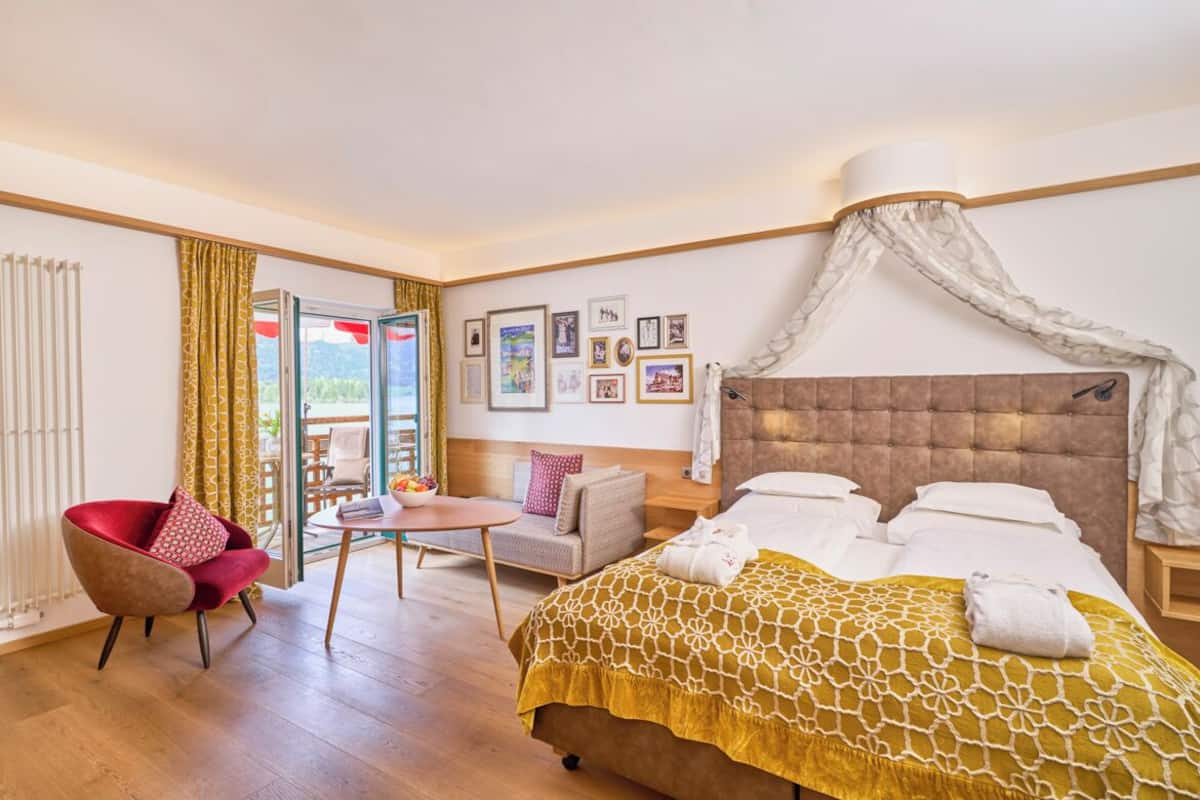 A hotel room with a bed, a chair, a table, and a balcony.