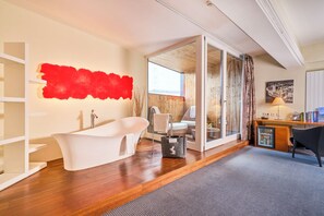 A modern bathroom with a freestanding bathtub, a glass shower enclosure, and a wooden desk with a chair. - Im Weissen Rössl am Wolfgangsee (Sankt Wolfgang im Salzkammergut)