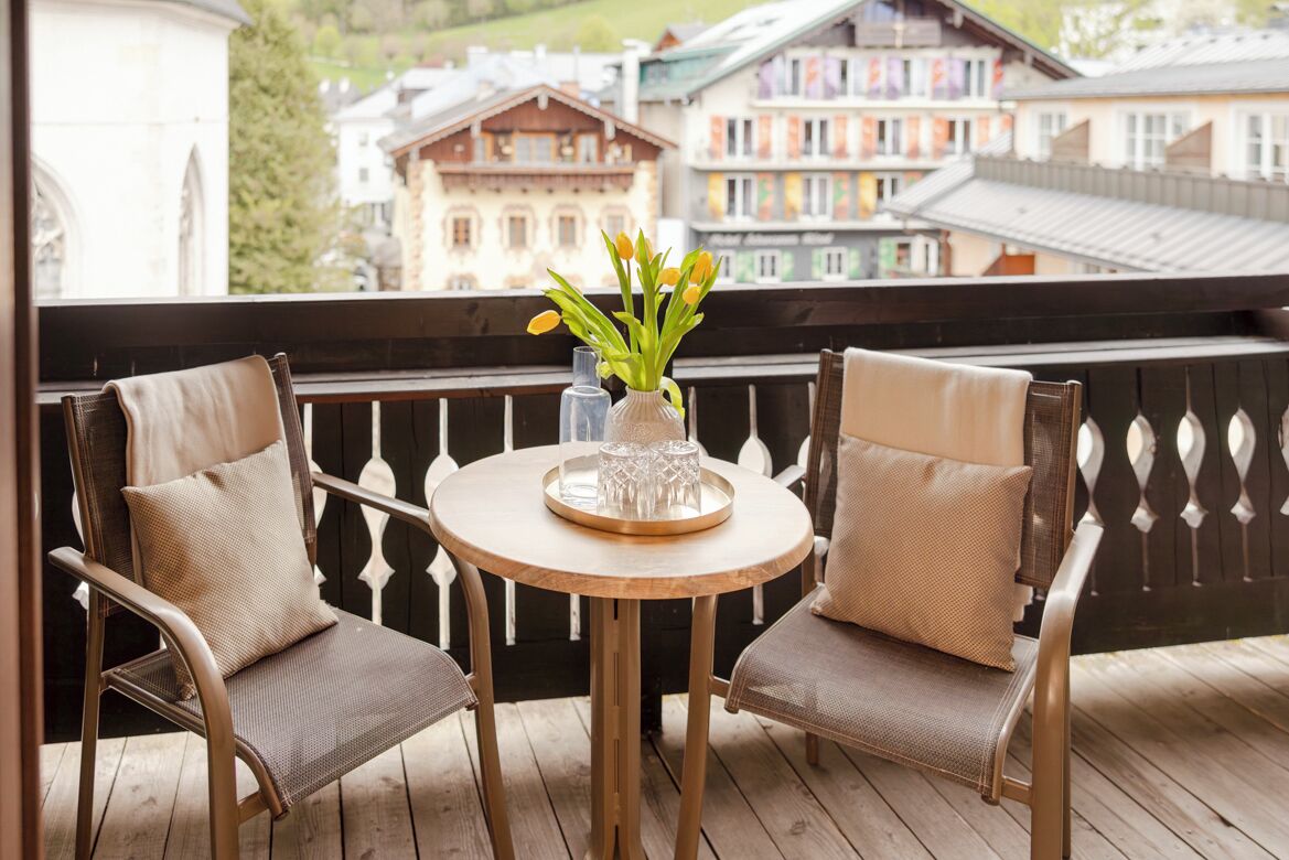 A balcony with two wicker chairs, a round wooden table, and a vase with flowers.