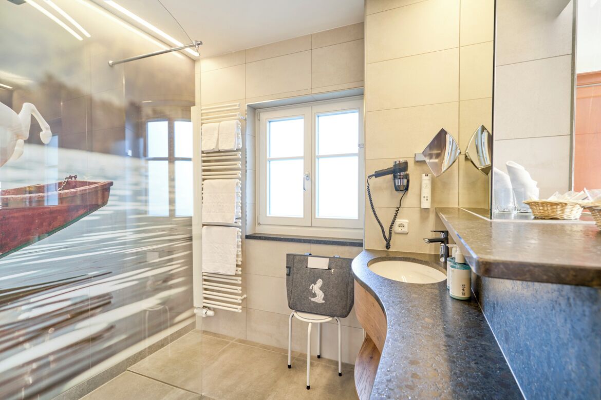 A modern bathroom with a large mirror, a sink, a towel rack, and a window.