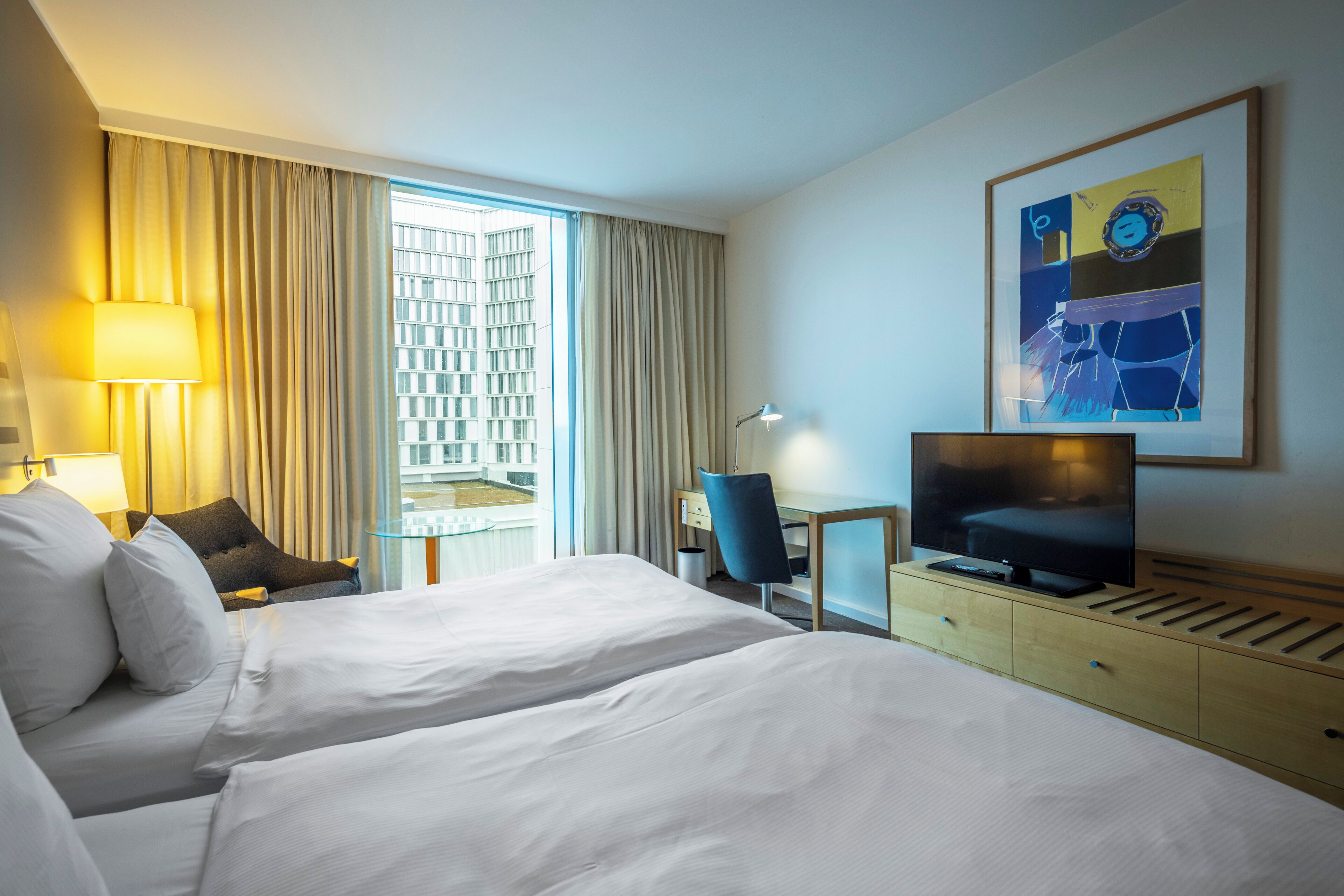 Une chambre d’hôtel avec deux lits, un bureau, une télévision et une grande fenêtre avec des rideaux.
