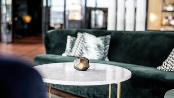 Un canapé vert agrémenté de coussins à motifs, une table ronde en marbre surmontée d’un porte-bougie en verre aux formes géométriques, et un aménagement intérieur moderne.