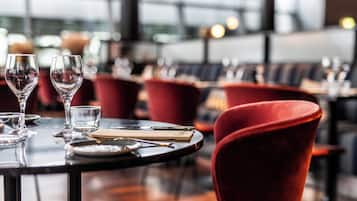 A restaurant setting with a table set for two, featuring red upholstered chairs and a glass wine glass.