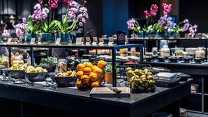 A buffet with various fruits and vegetables, including oranges and bananas, and decorative orchids in blue vases. - Clarion Hotel Copenhagen Airport (Kastrup)