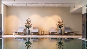 A modern indoor pool area with two lounge chairs and vases of flowers, reflecting on the pool's surface. - Clarion Hotel Copenhagen Airport (Kastrup)