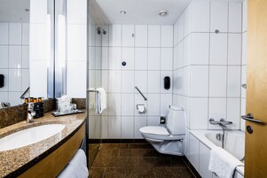 Un baño moderno con lavamanos de granito, inodoro blanco, bañera y ducha.